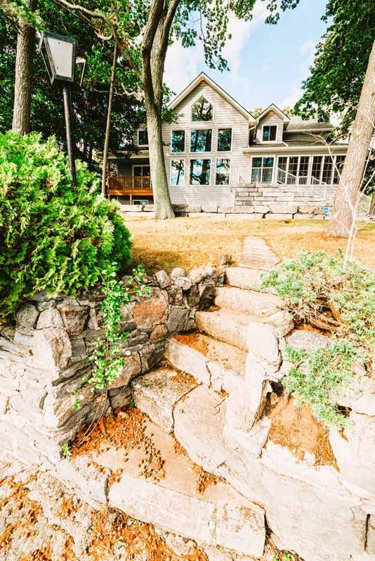 Stone steps lead to a white house with large windows, framed by trees and a landscaped yard.