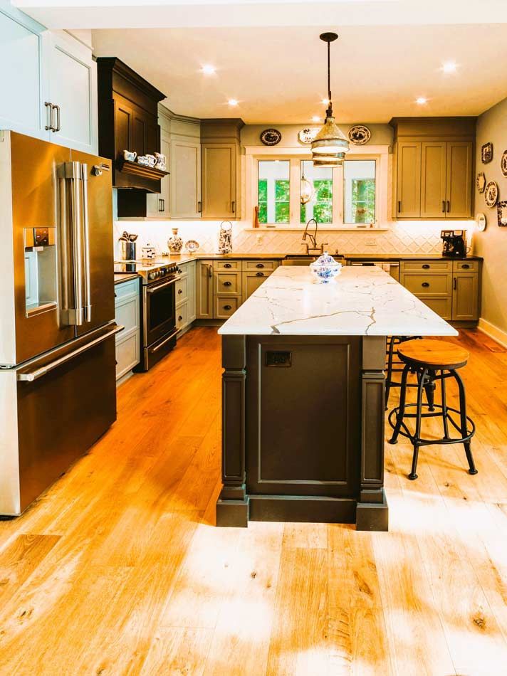 Bright kitchen with a large island, stainless fridge, wood floors, and bar stools under pendant lights