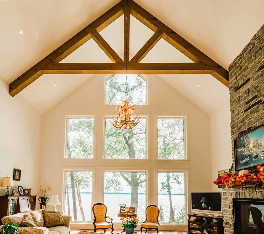 Bright living room with vaulted wooden beams, large windows, stone fireplace, and chandelier
