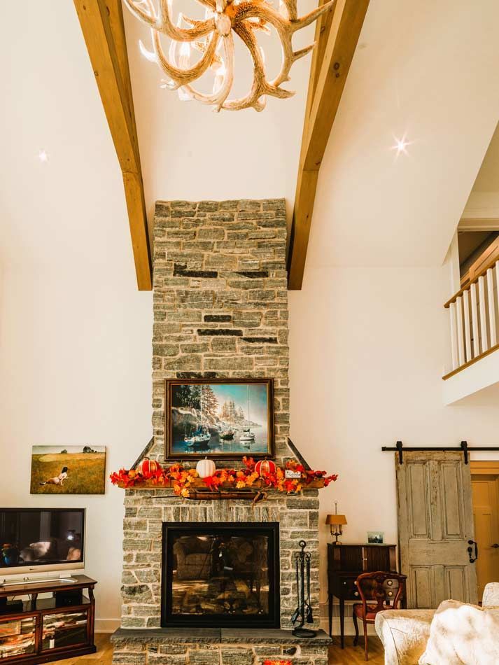Living room with tall stone fireplace, festive garland, vaulted ceiling, and chandelier