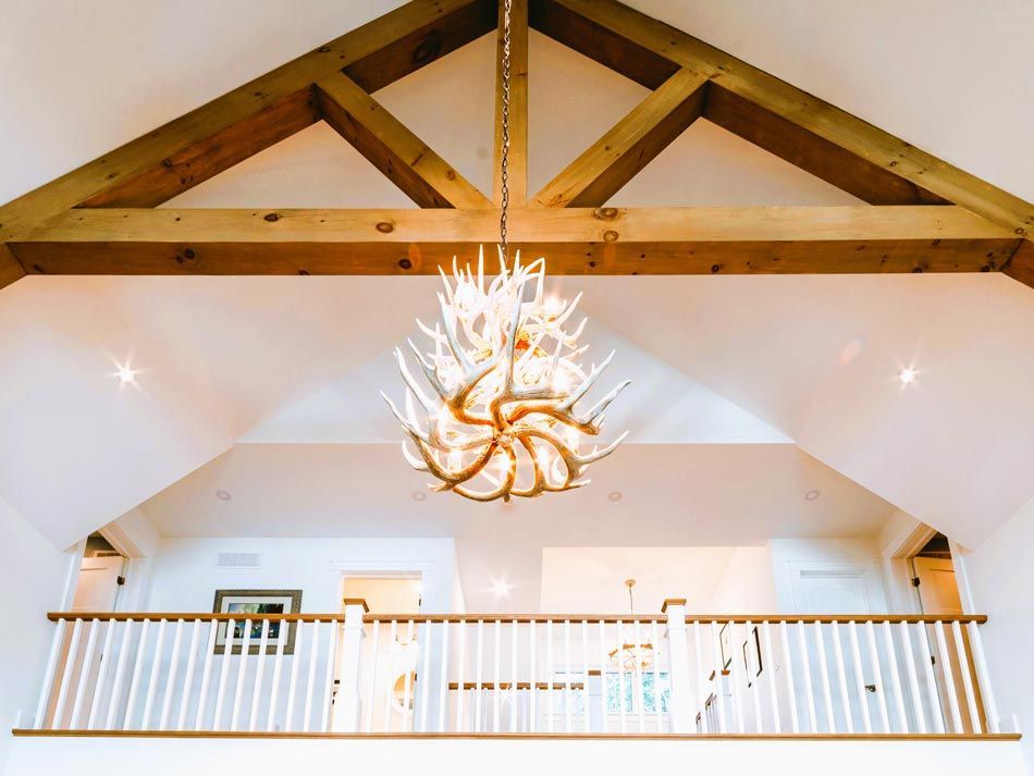 Loft interior with exposed wood beams, white balcony railing, and a large chandelier hanging center