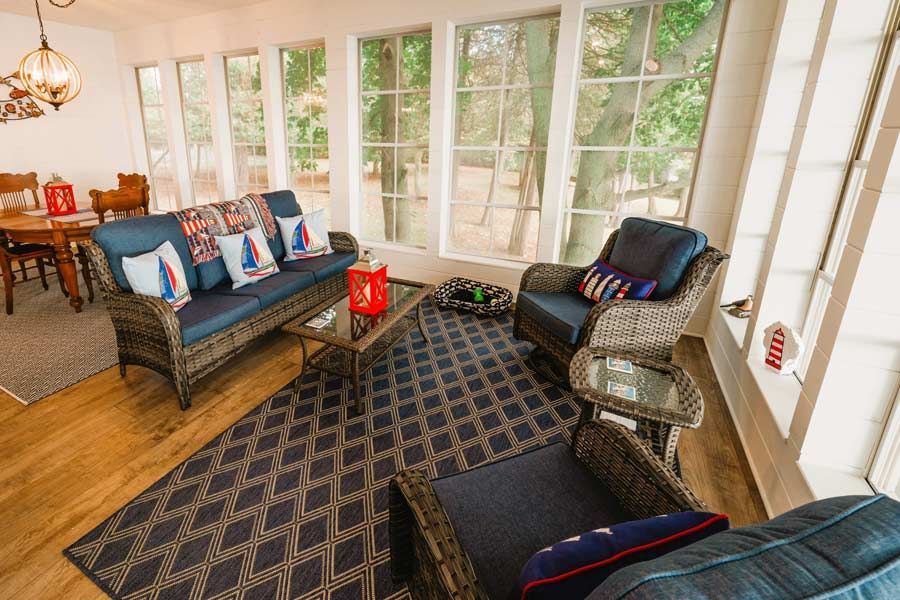 Sunroom with wicker seating, patterned rug, and large windows overlooking greenery