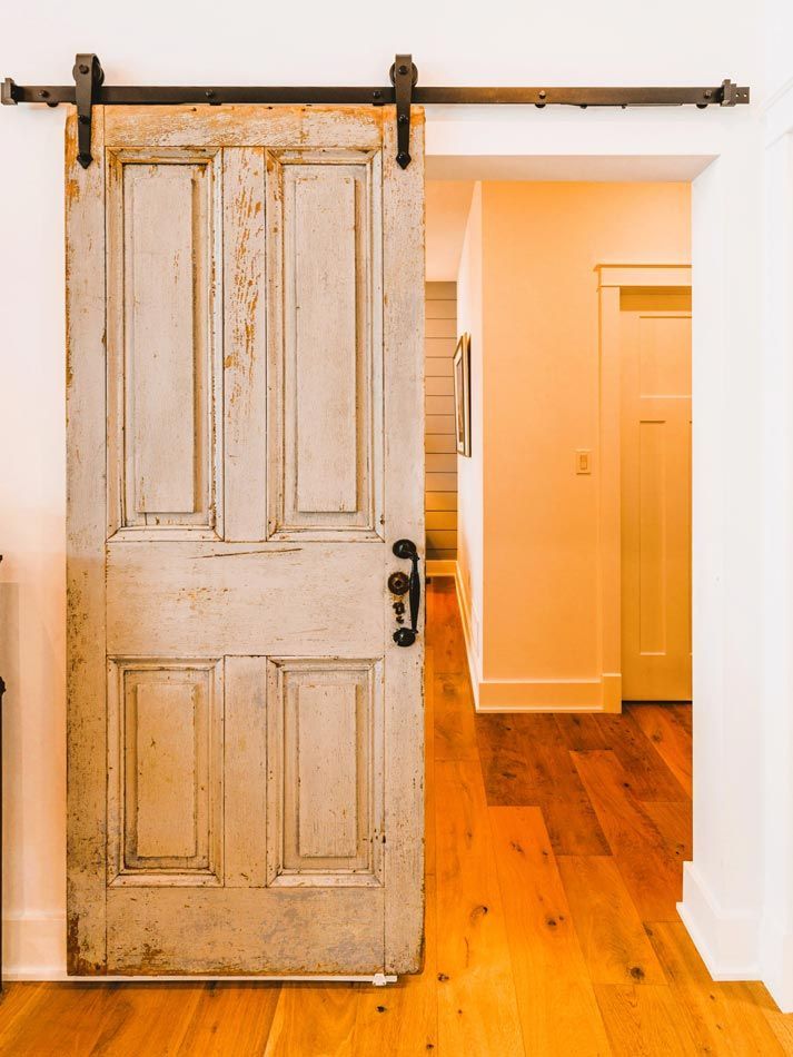 Rustic white sliding door on black track opening to a warm hallway with wood floors