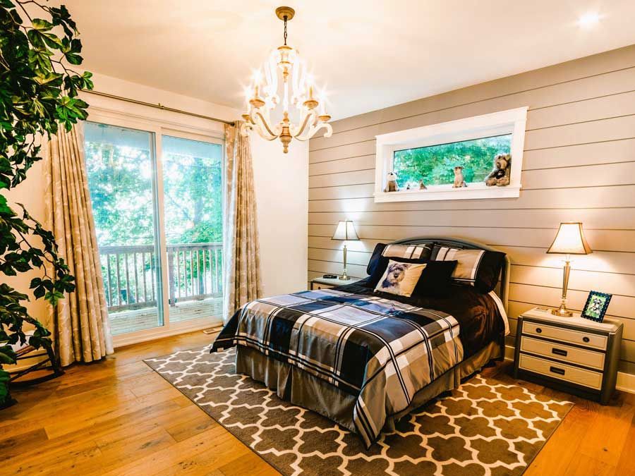 Cozy bedroom with king bed, chandelier, wood floors, balcony doors, and warm neutral decor