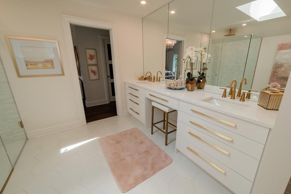 Bright white bathroom vanity with gold fixtures, large mirror, pink rug, and skylight.