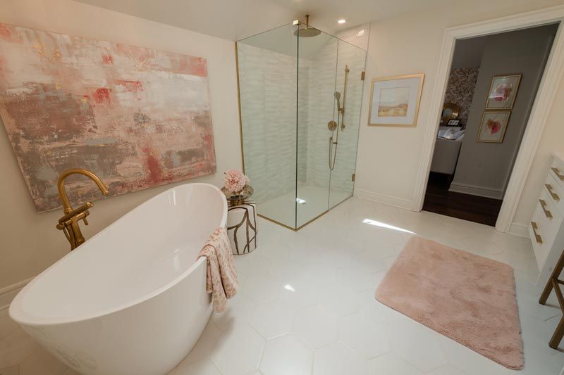 Bright modern bathroom with freestanding tub, glass shower, large wall art, and soft pink rug.