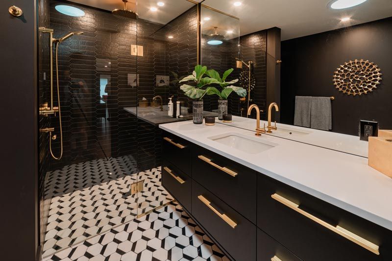 Modern black bathroom with white vanity, gold fixtures, patterned floor, and glass shower enclosure