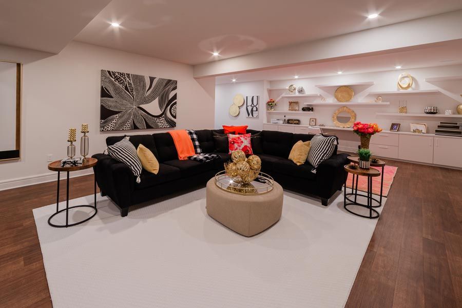 Modern living room with black sofas, white rug, coffee table, and open kitchen shelves
