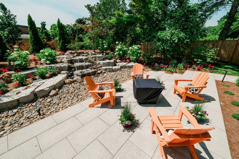 Patio with orange chairs around a fire pit, stone steps, and lush garden landscaping