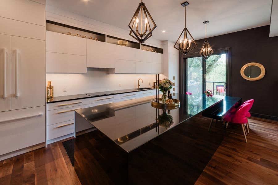 Modern kitchen with black island, white cabinets, pendant lights, and a dining table by large windows