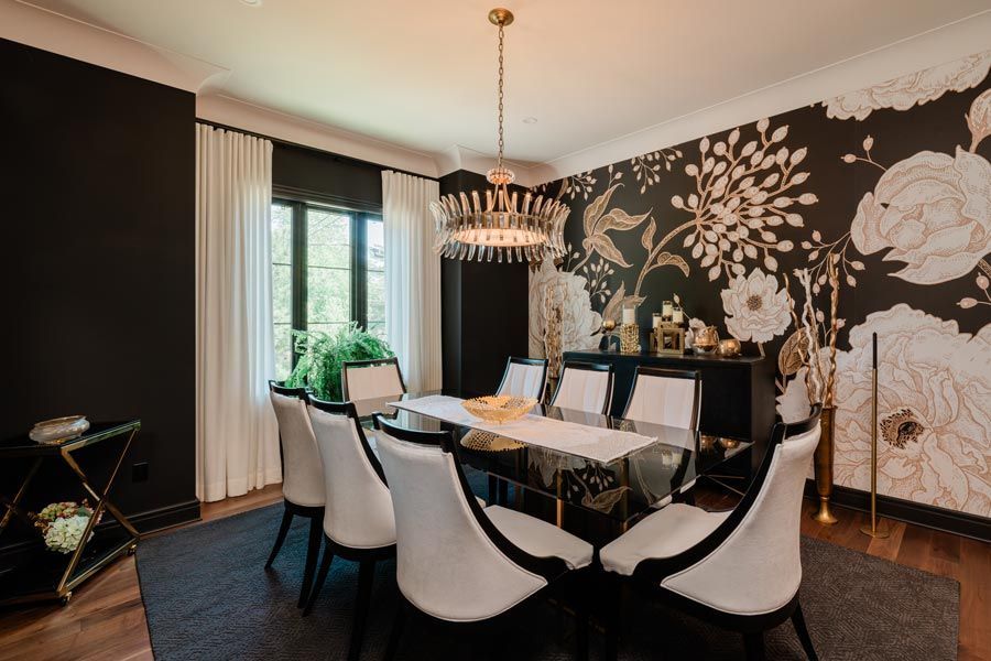 Elegant dining room with black floral wallpaper, white chairs, glass table, and chandelier