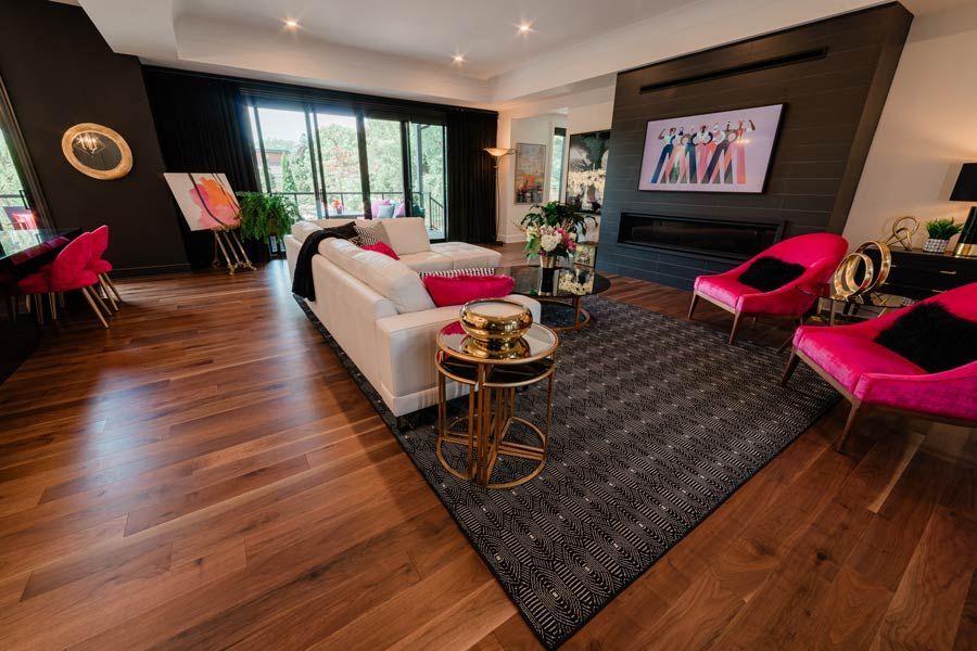 Modern living room with hardwood floors, white sofa, hot pink chairs, dark rug, and large windows