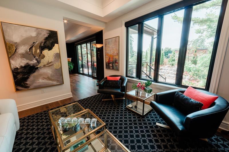 Modern living room with black sofa, glass tables, abstract art, and large windows overlooking greenery