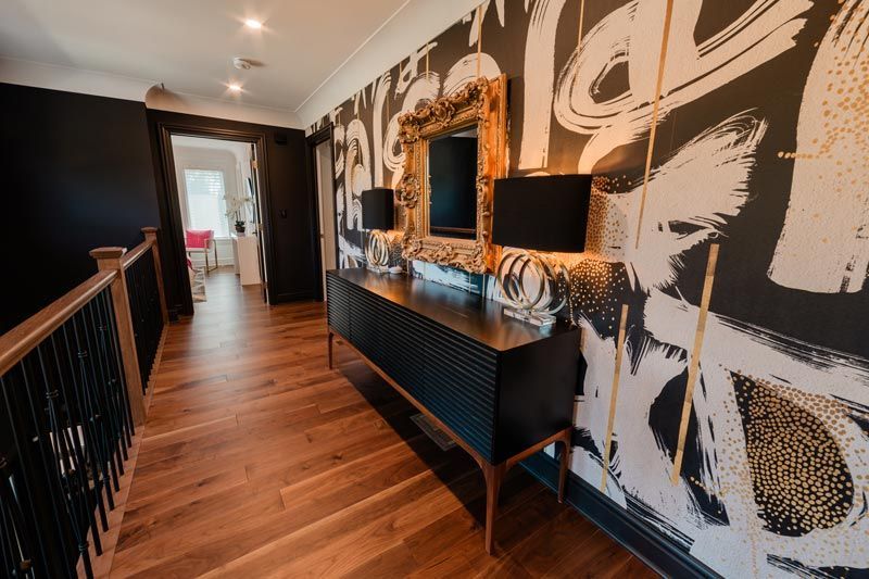 Hallway with wood floors, black-and-white abstract wall mural, and a console table with mirror and lamp