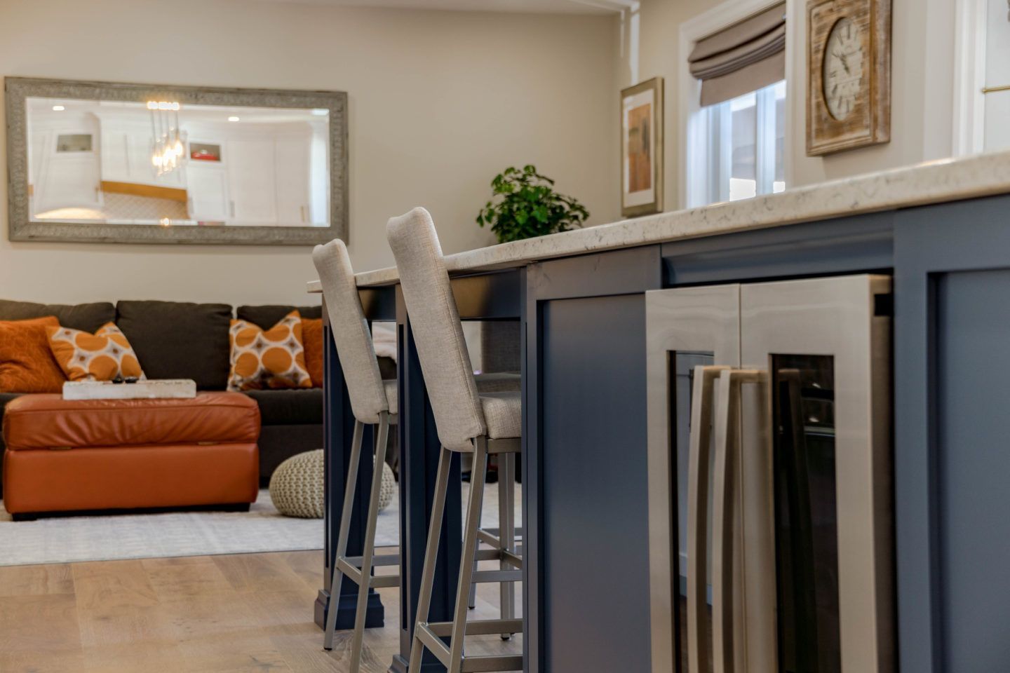 Modern kitchen island with bar stools overlooking a living room with an orange sofa and wall art
