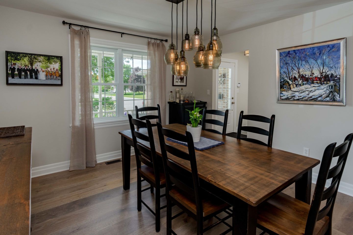 Dining room with dark wood table, black chairs, pendant lights, and windows with sheer curtains