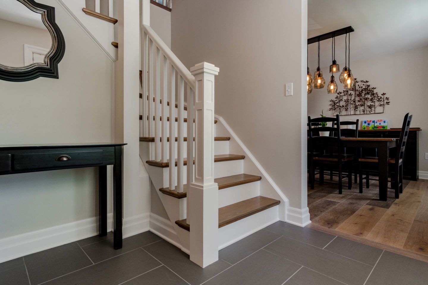 Interior staircase beside dining area with white railing, dark tile floor, and black table with pendant lights