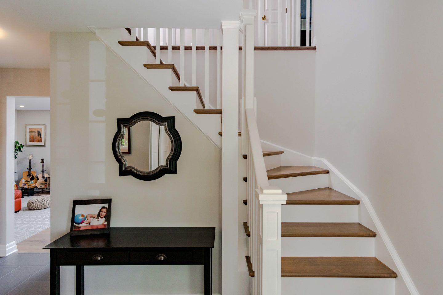 Staircase with white railing, wood steps, and a black console table in a bright entryway.