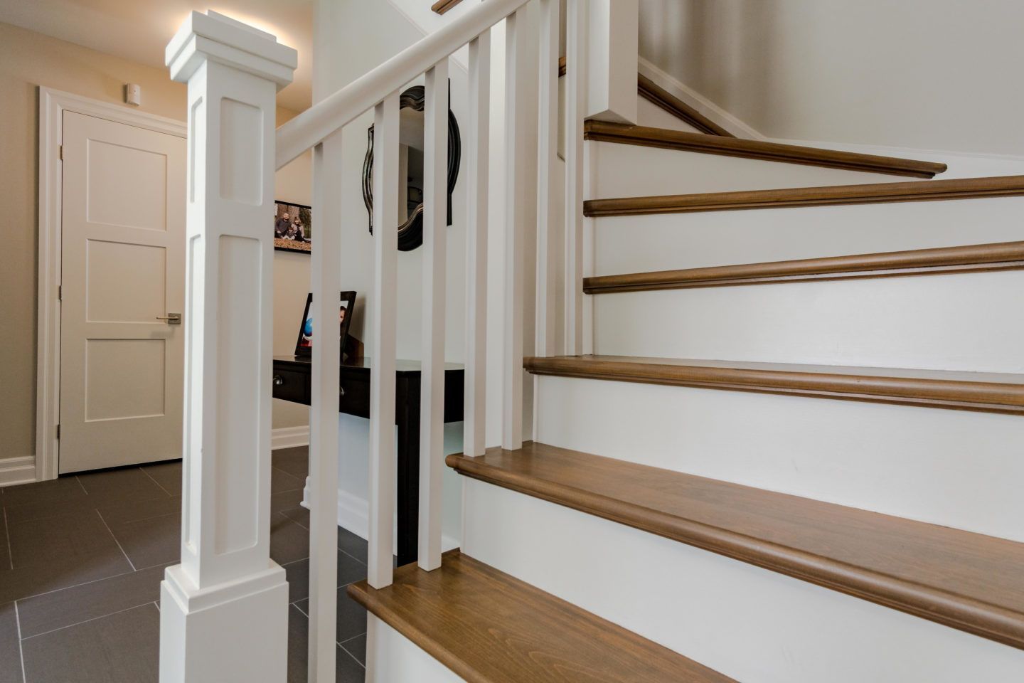 Staircase with white balusters and wooden handrail, viewed from a hallway with a closed door