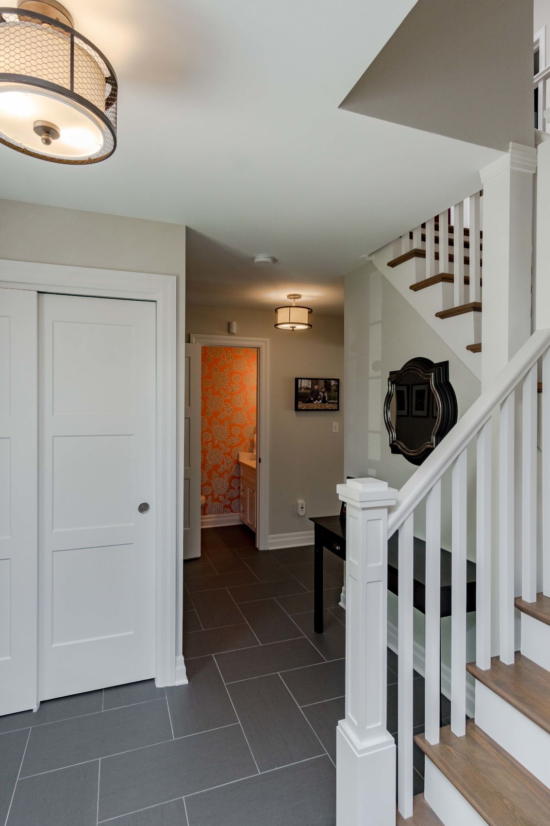 Bright entryway with white staircase, closet doors, gray tile floor, and hanging ceiling lights.