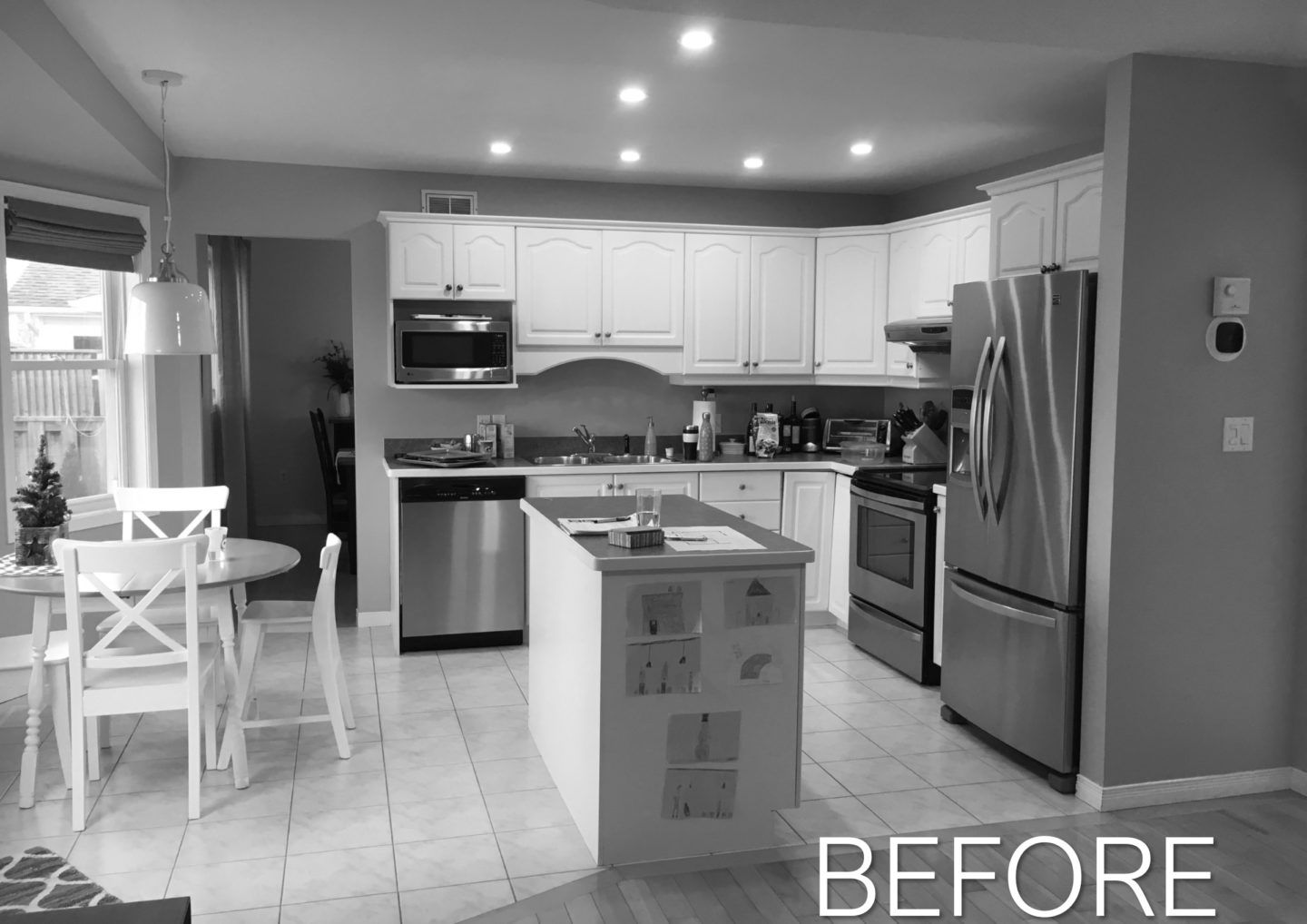 Kitchen before renovation with white cabinets, stainless appliances, central island, and dining table by window