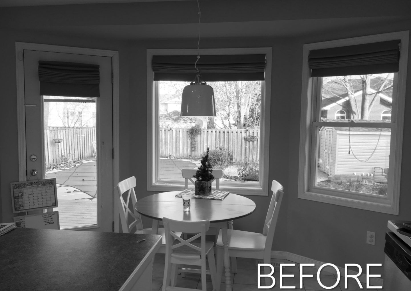 Black-and-white view of a dining nook with round table, chairs, and three windows.
