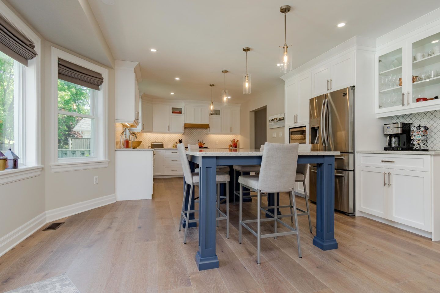 Bright modern kitchen with island, stainless fridge, white cabinets, and light wood floors