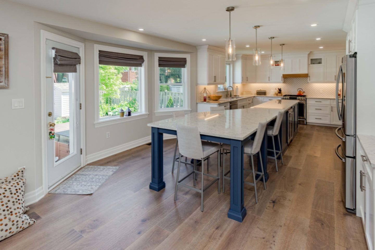Bright modern kitchen with a large island, barstools, stainless appliances, and bay windows.