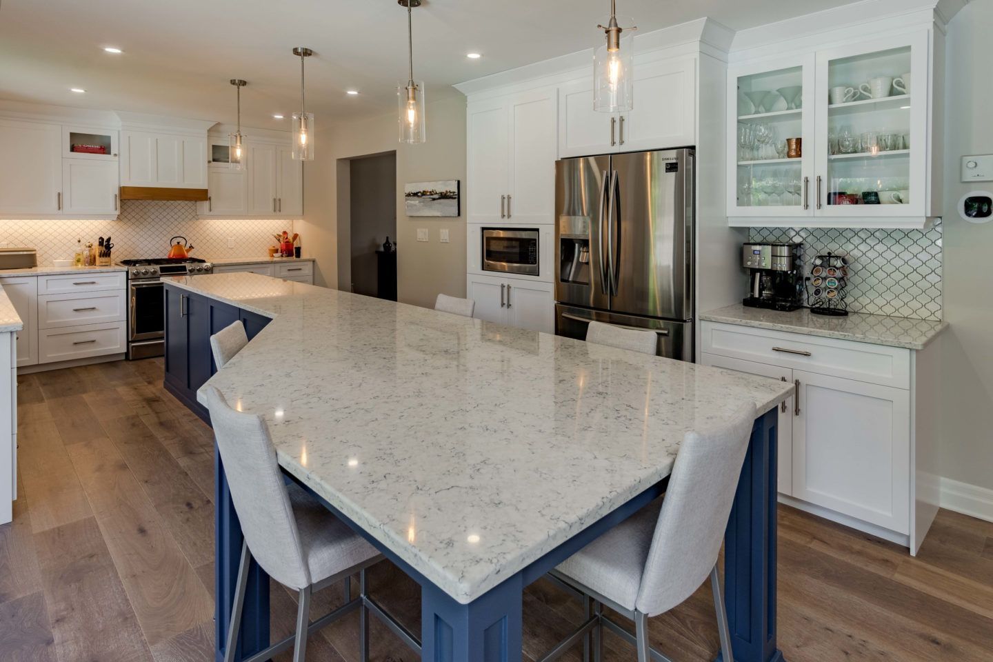 Modern kitchen with large marble island, white cabinets, stainless steel appliances, and pendant lights