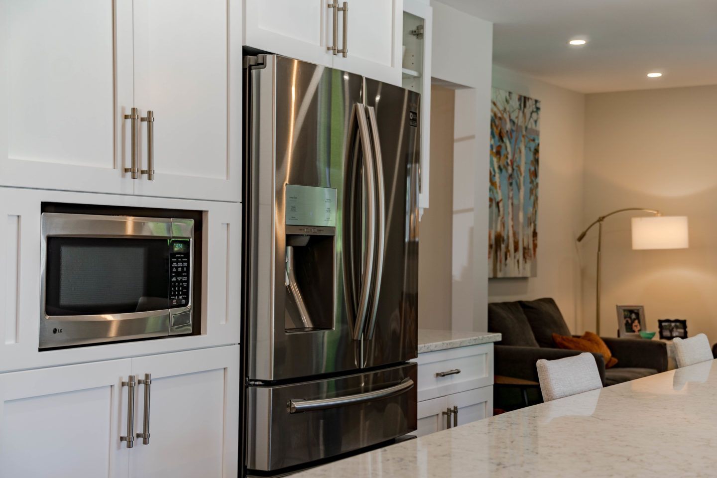 Modern white kitchen with stainless steel refrigerator, built-in microwave, and island seating