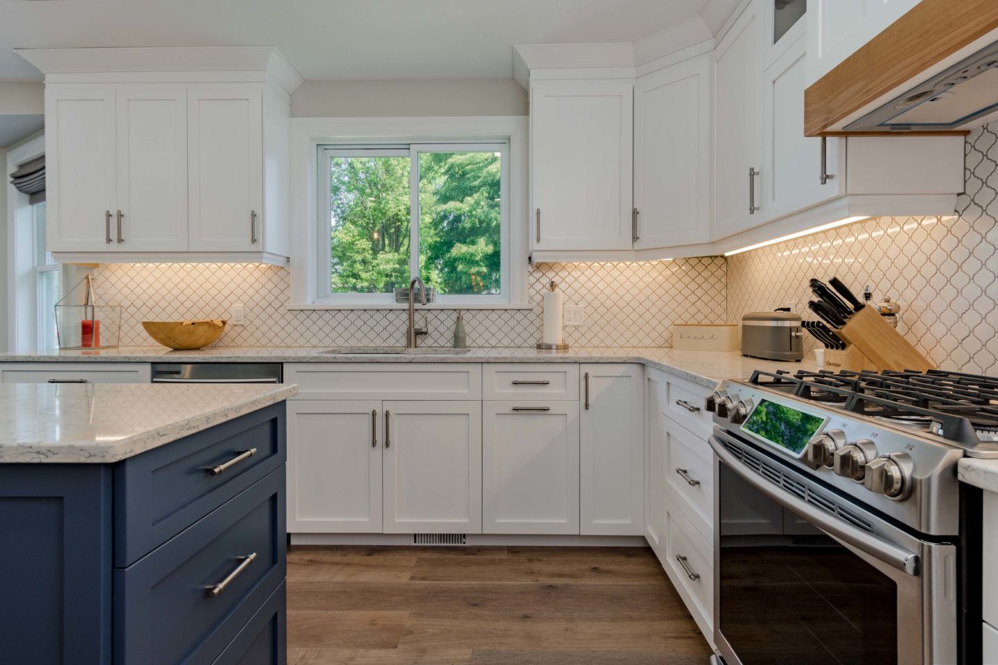 Bright white kitchen with navy island, stainless stove, and sunlit window over sink.