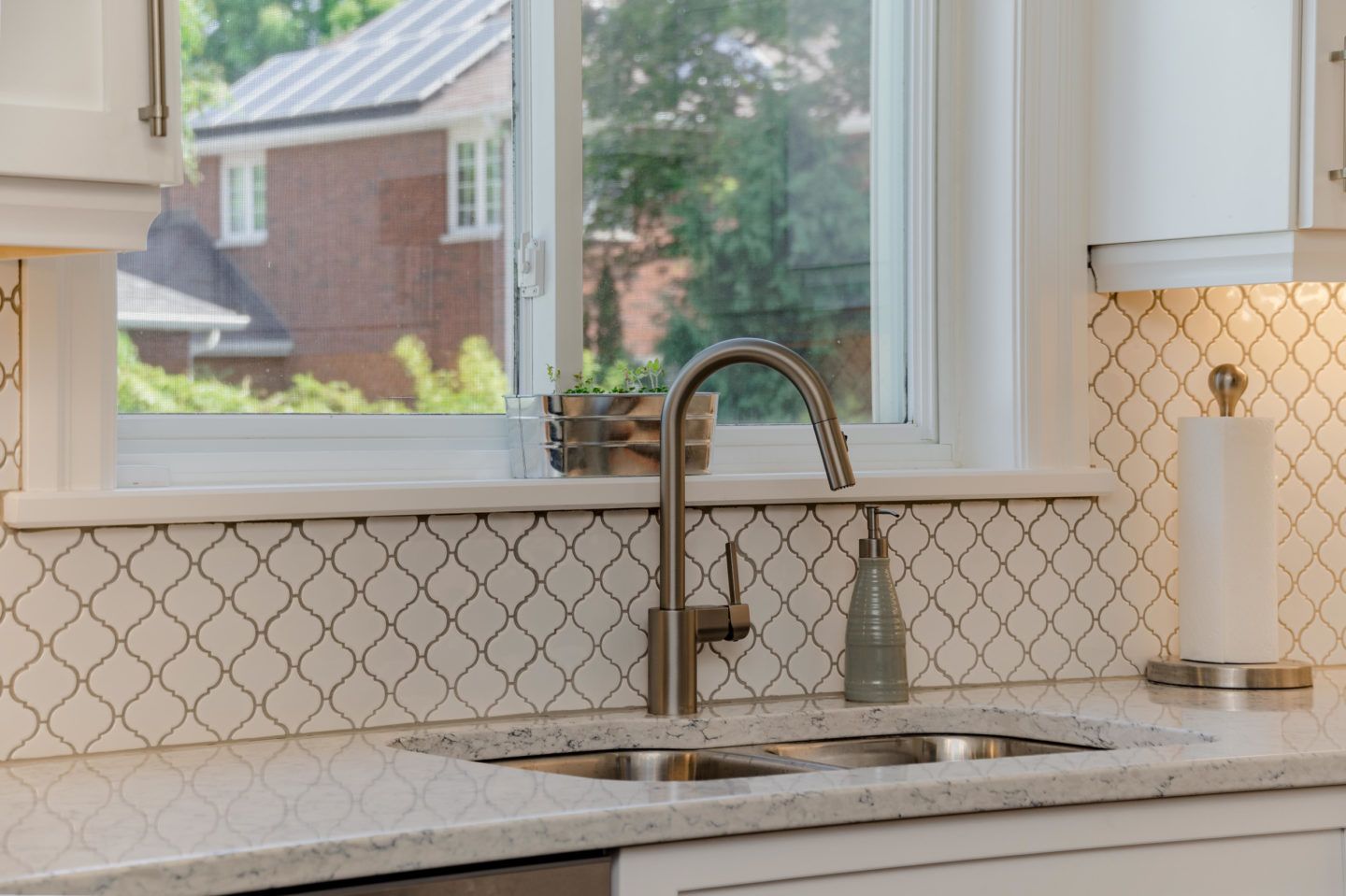 Kitchen sink below window with patterned backsplash and modern faucet, lit by daylight