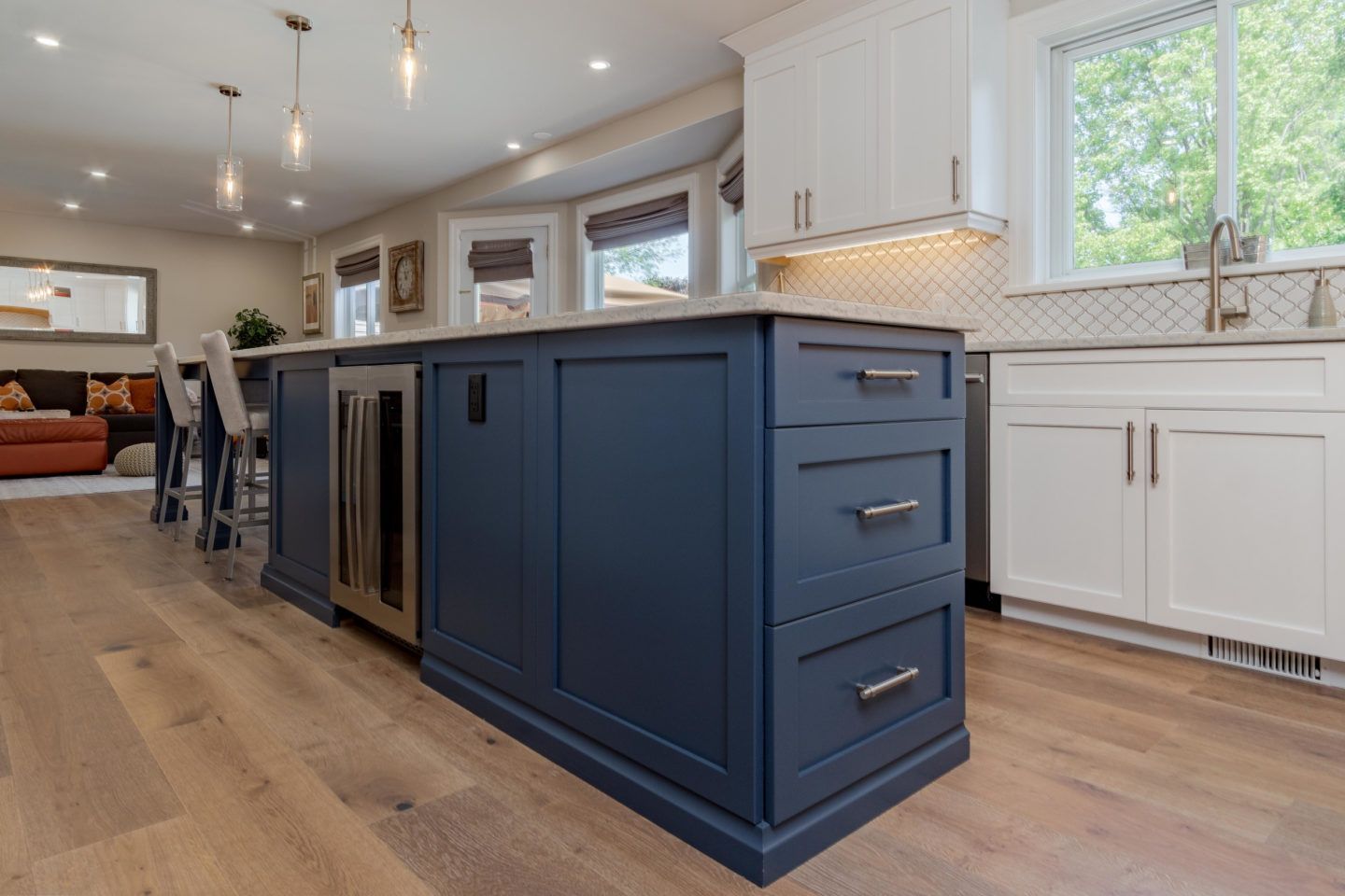 Modern kitchen with a navy-blue island, white cabinets, wood floors, and bright windows