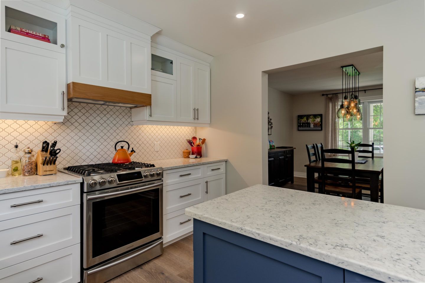 Modern white kitchen with stainless steel oven, blue island, and adjacent dining area