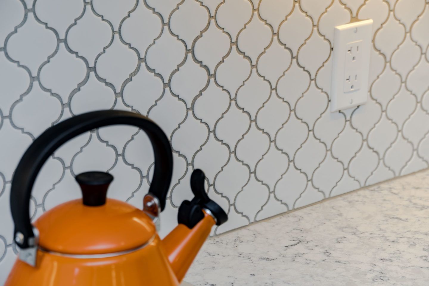 Orange kettle on a countertop beside a tiled wall and electrical outlet