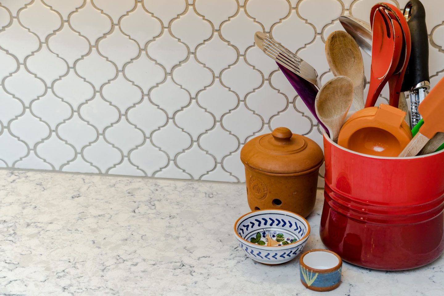 Kitchen counter with red utensil holder, wooden canister, and small bowls against a patterned backsplash