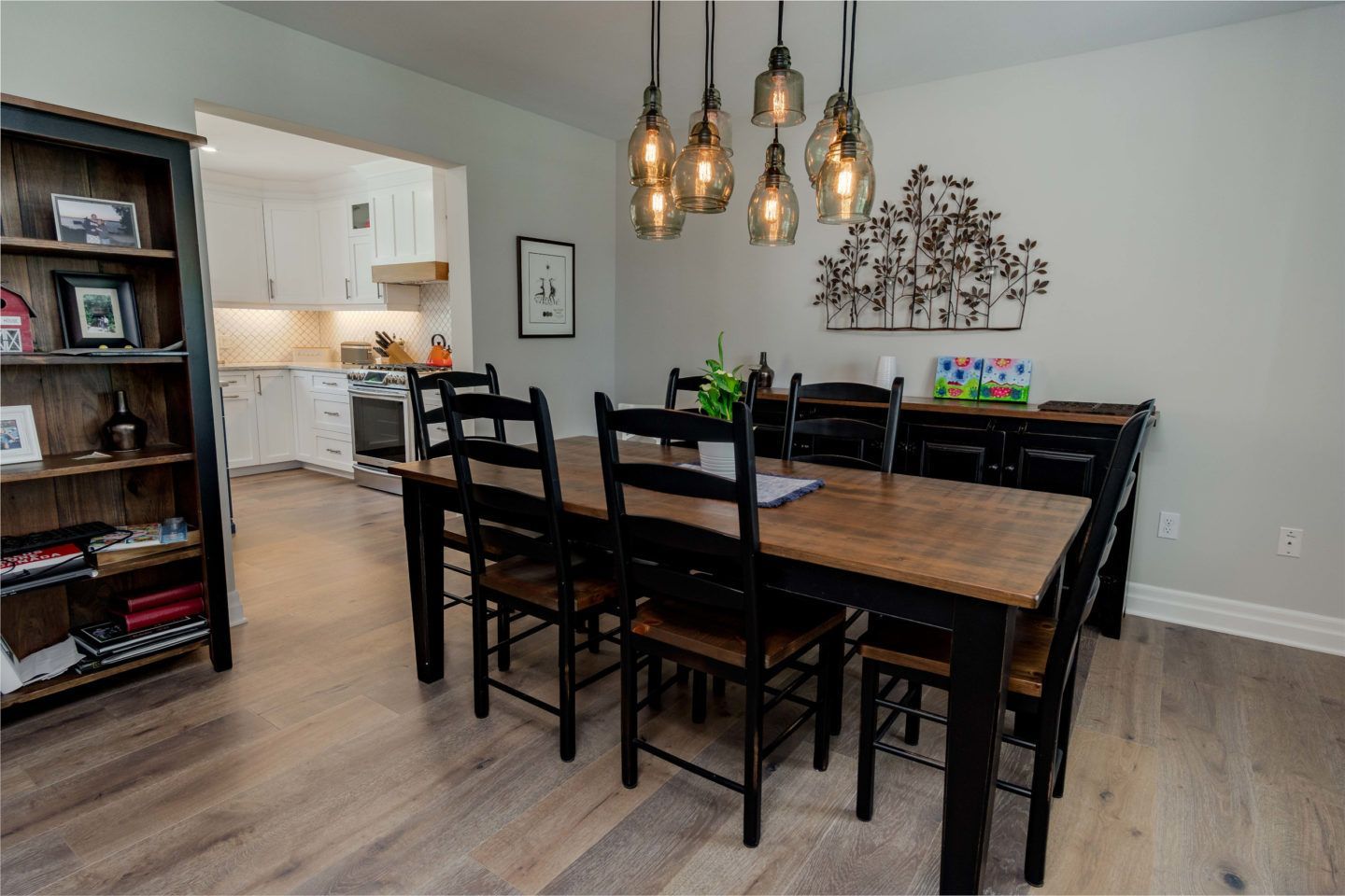 Dining room with dark wood table and chairs, pendant lights, and kitchen visible in the background