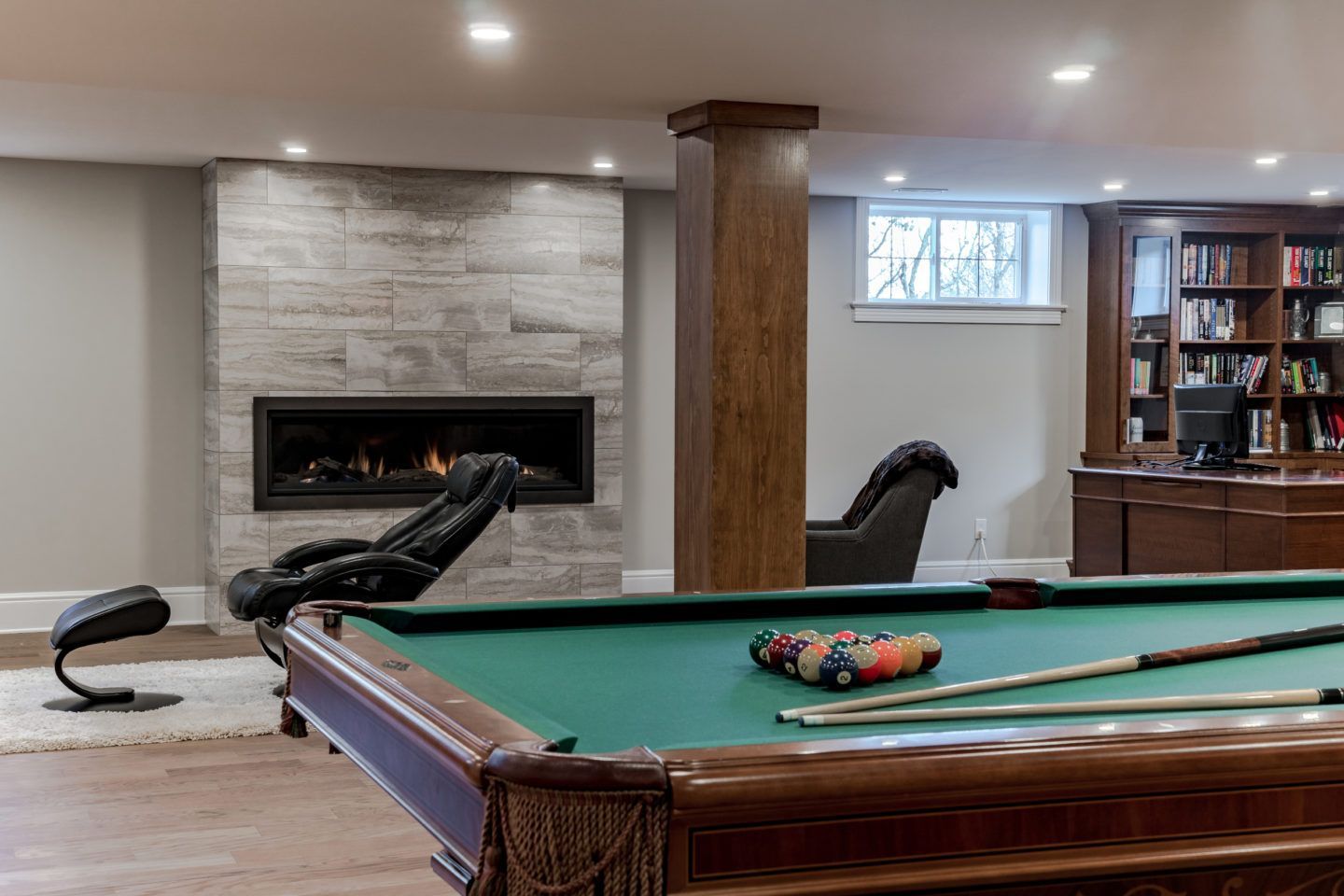 Basement game room with pool table, leather chaise, fireplace, and bookshelves