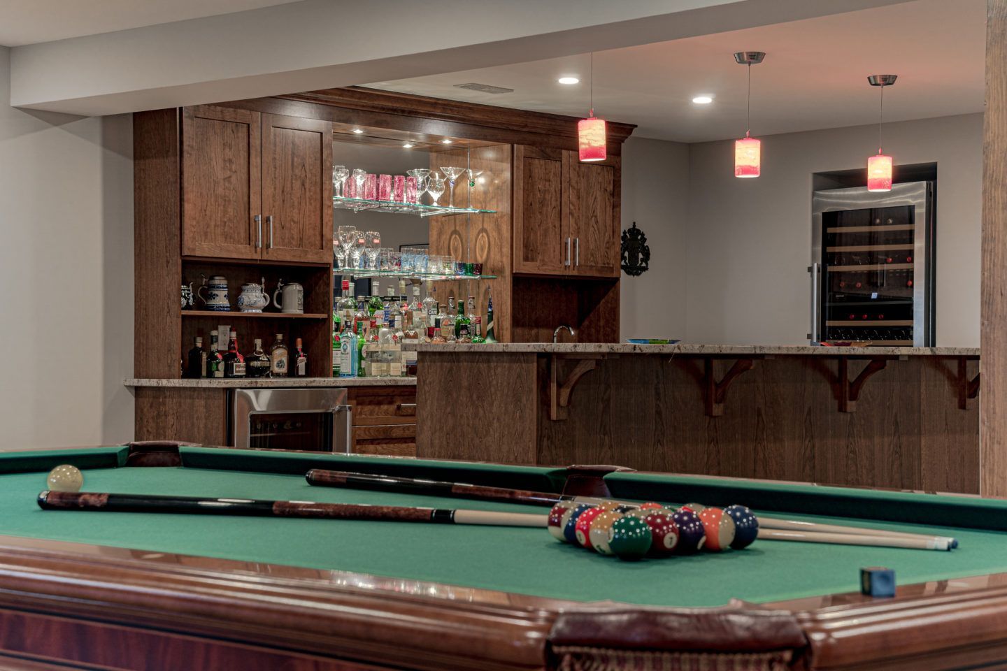 Pool table in a bar with cue sticks and a rack of balls, wooden bar and glass shelves in the background