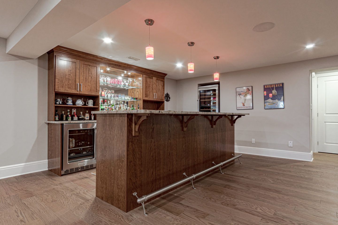 Spacious home bar with dark wood counter, glass shelves, and recessed lighting in a finished basement