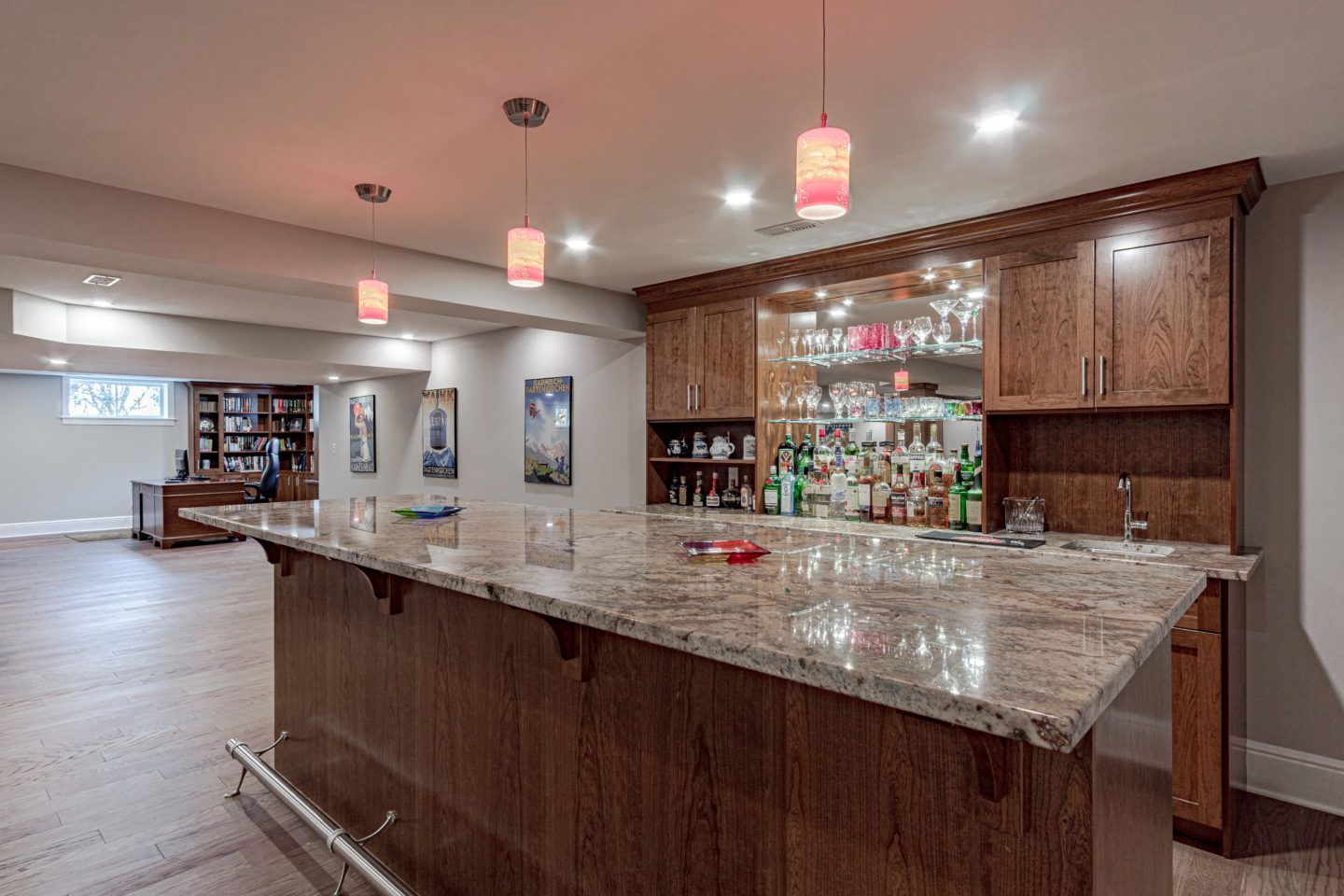 Spacious home bar with granite countertop, wood cabinets, pendant lights, and mirrored liquor shelves