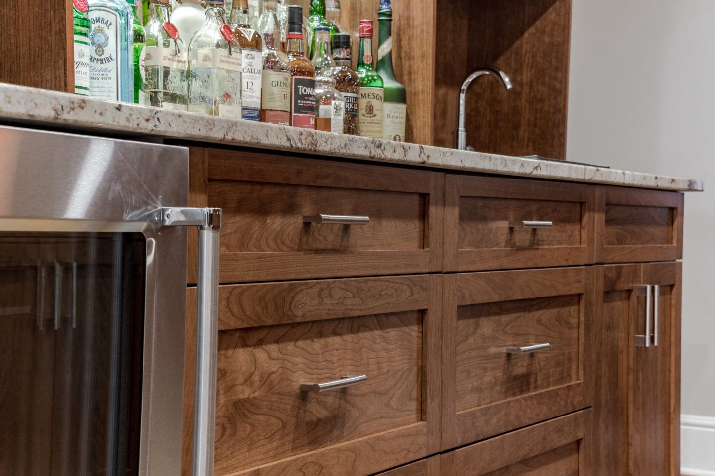 Wooden kitchen island with drawers, stainless steel appliance, and bottles on a granite countertop