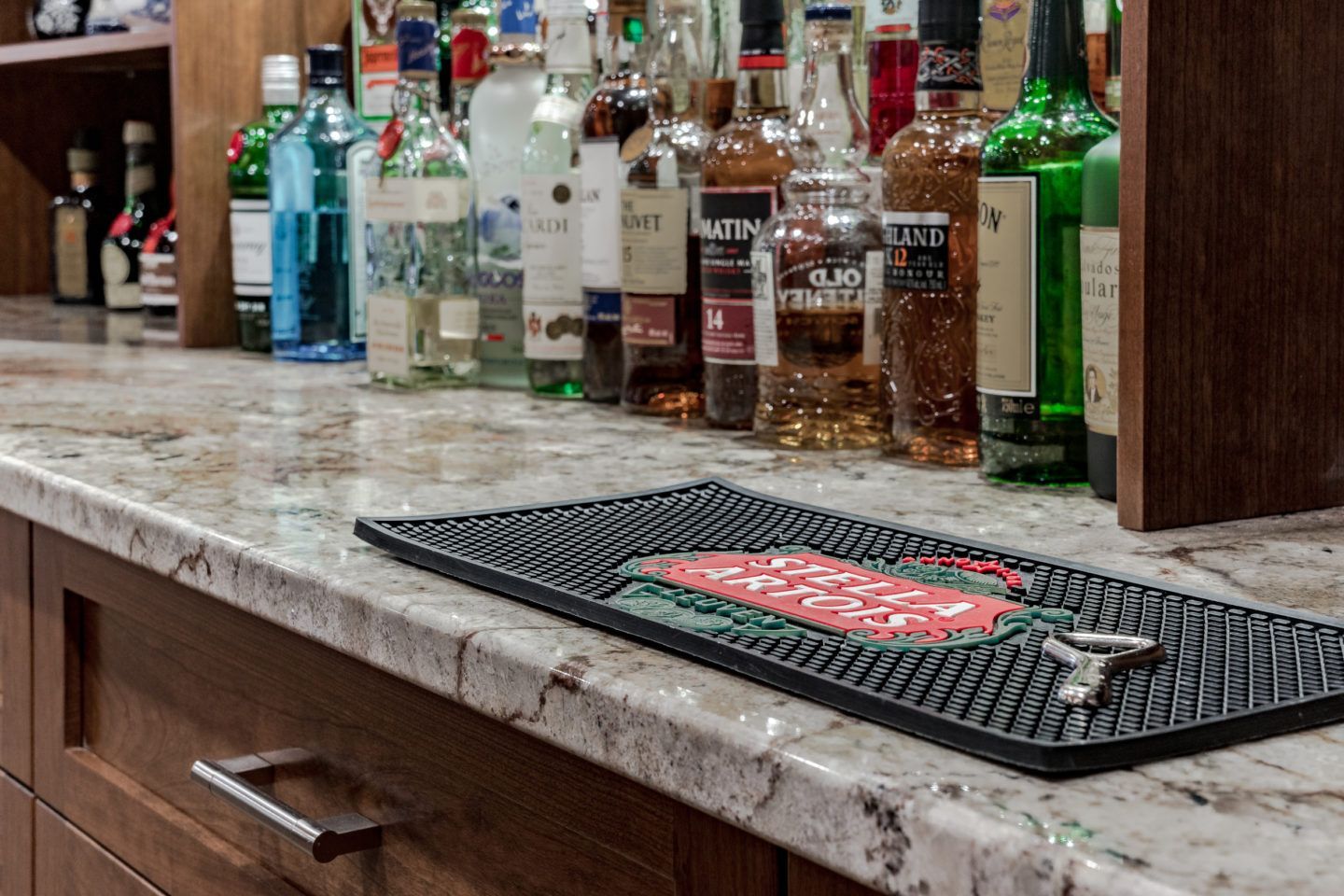 Bar counter with assorted liquor bottles and a bar mat on a marble countertop.