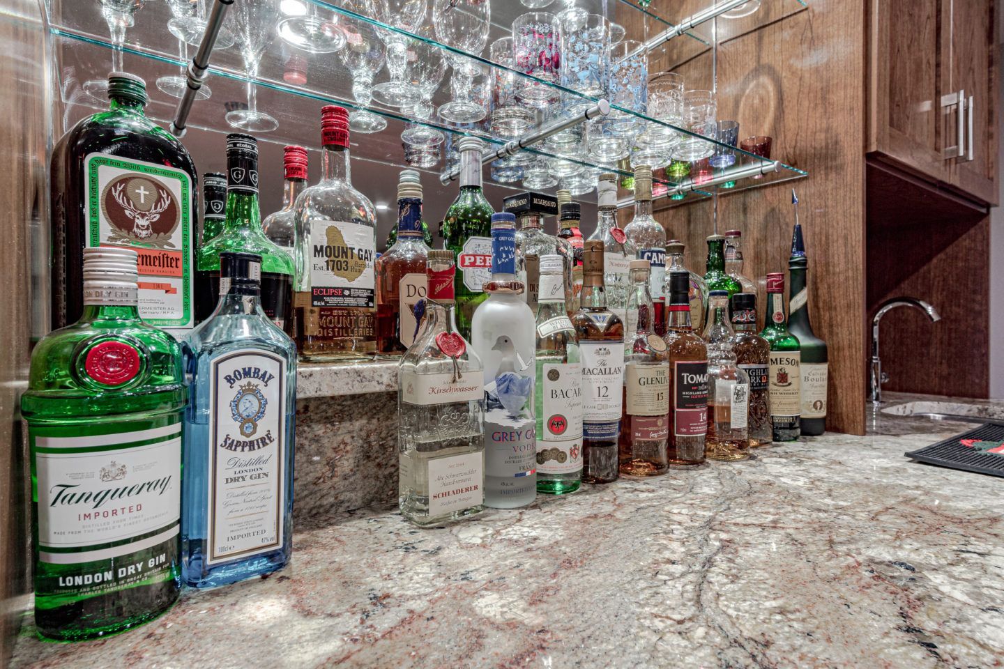 Assorted liquor bottles arranged on a stone counter in a mirrored bar area
