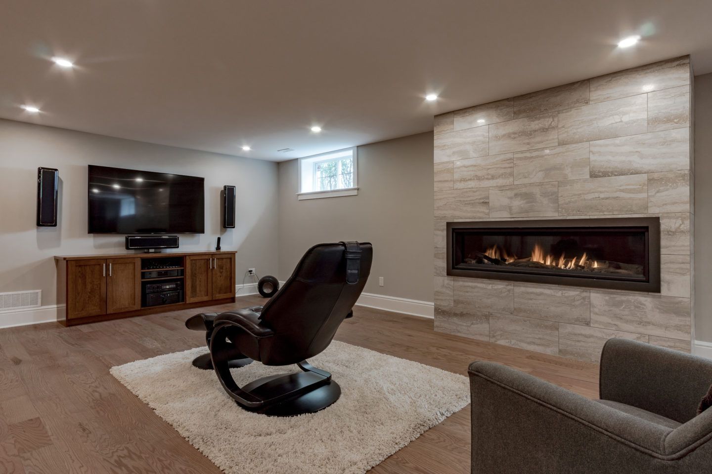 Modern living room with a wall-mounted TV, fireplace, recliner, and sectional sofa on a rug.