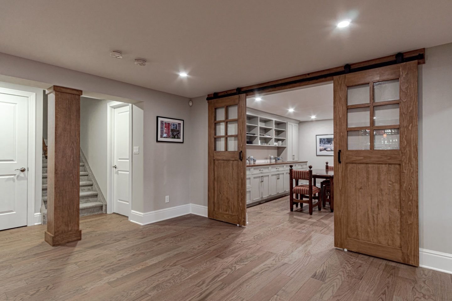 Basement rec room with wood floors, sliding barn doors, and a small dining area beyond.