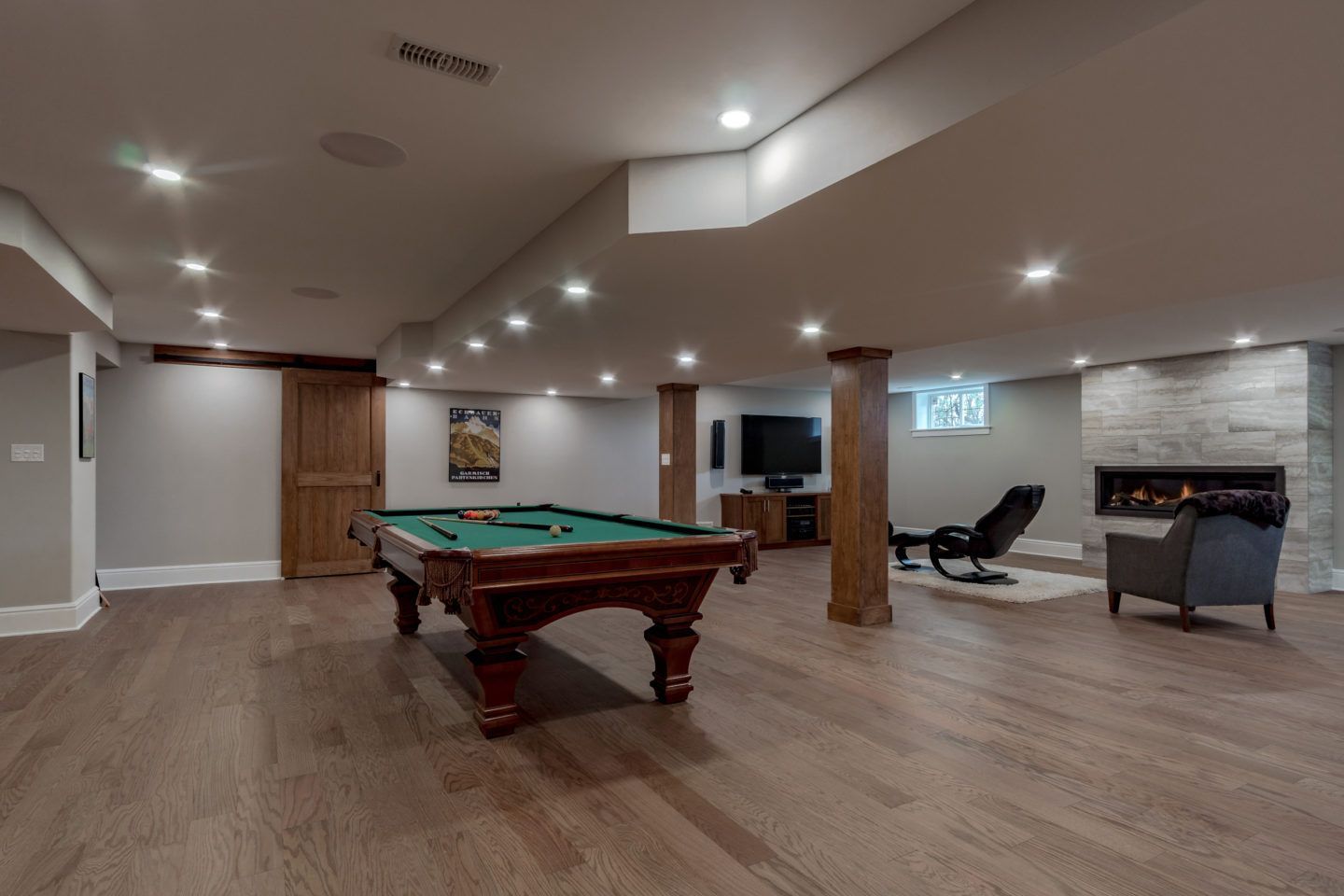 Finished basement with a pool table, lounge chairs, TV, and wood flooring