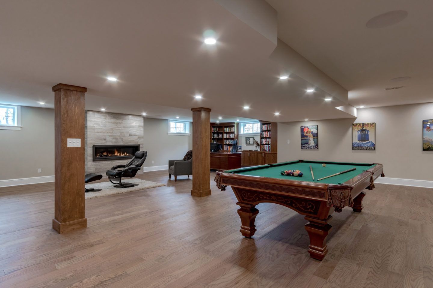 Spacious basement game room with pool table, massage chair, wooden columns, and recessed lighting