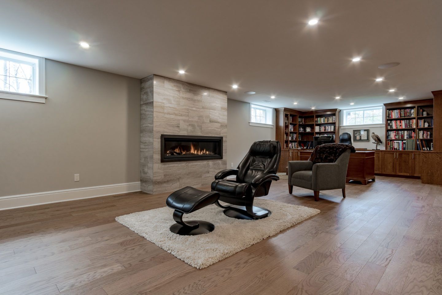 Spacious basement living room with a fireplace, recliner, chairs, bookshelves, and recessed lighting