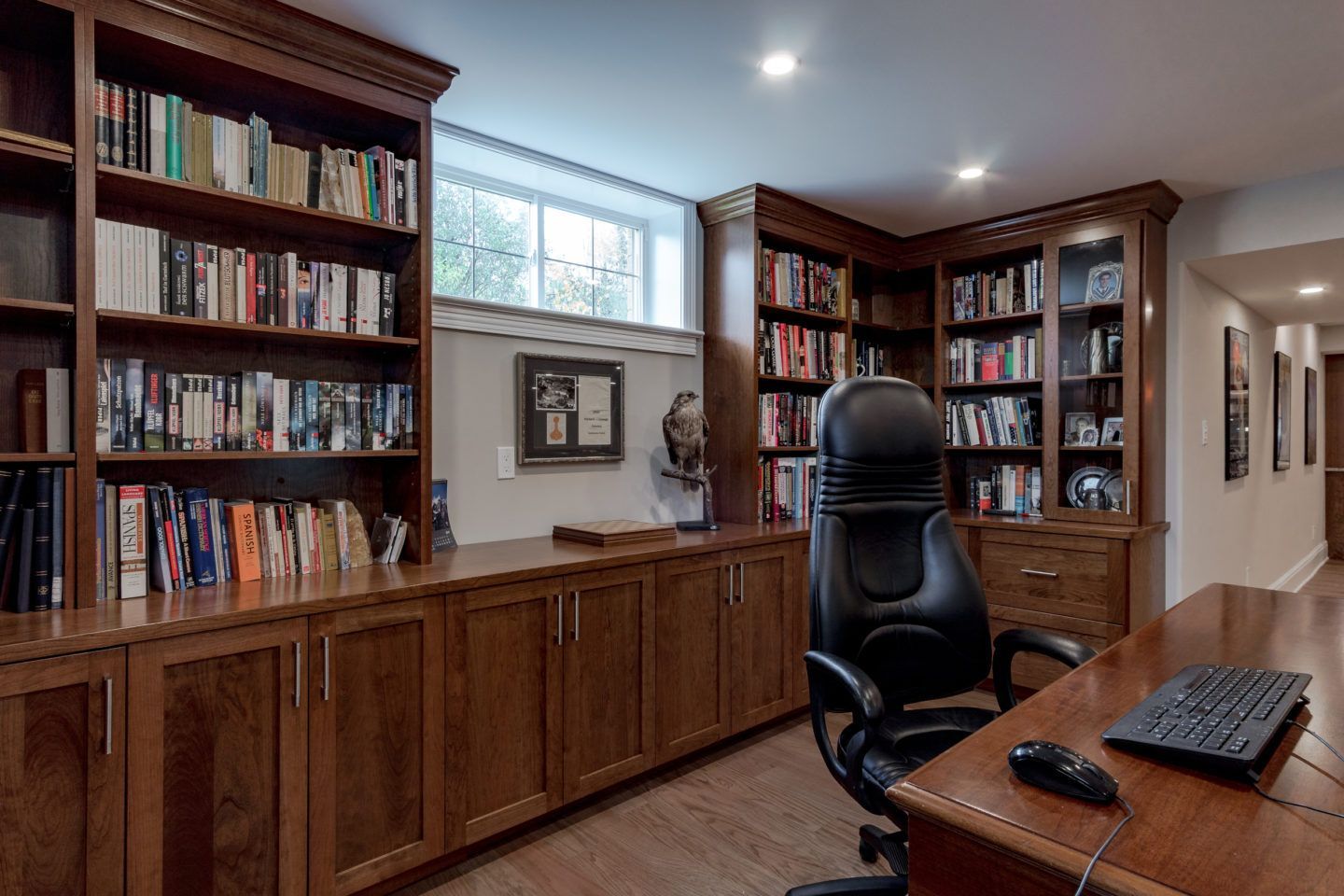 Wood-paneled home office with bookshelves, a desk, and a black office chair by a window.